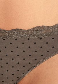 Grijze lingerie met stippen en kantafwerking, met kleine zwarte stippen en een soepele textuur. De tailleband heeft een geschulpte kantafwerking.