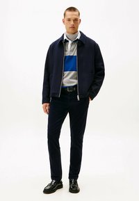 Granatowa bluza na zamek, szary shirt z niebieskim paskiem, ciemne spodnie i czarne buty. Gładka tkanina, nowoczesny design i dopasowany krój.