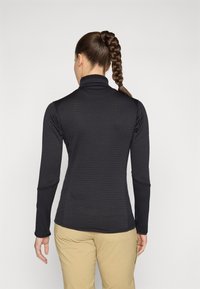 Zwarte top met lange mouwen en hoge kraag, voorzien van een textuurpatroon, slim fit en platte naden. Draagt met beige broek.