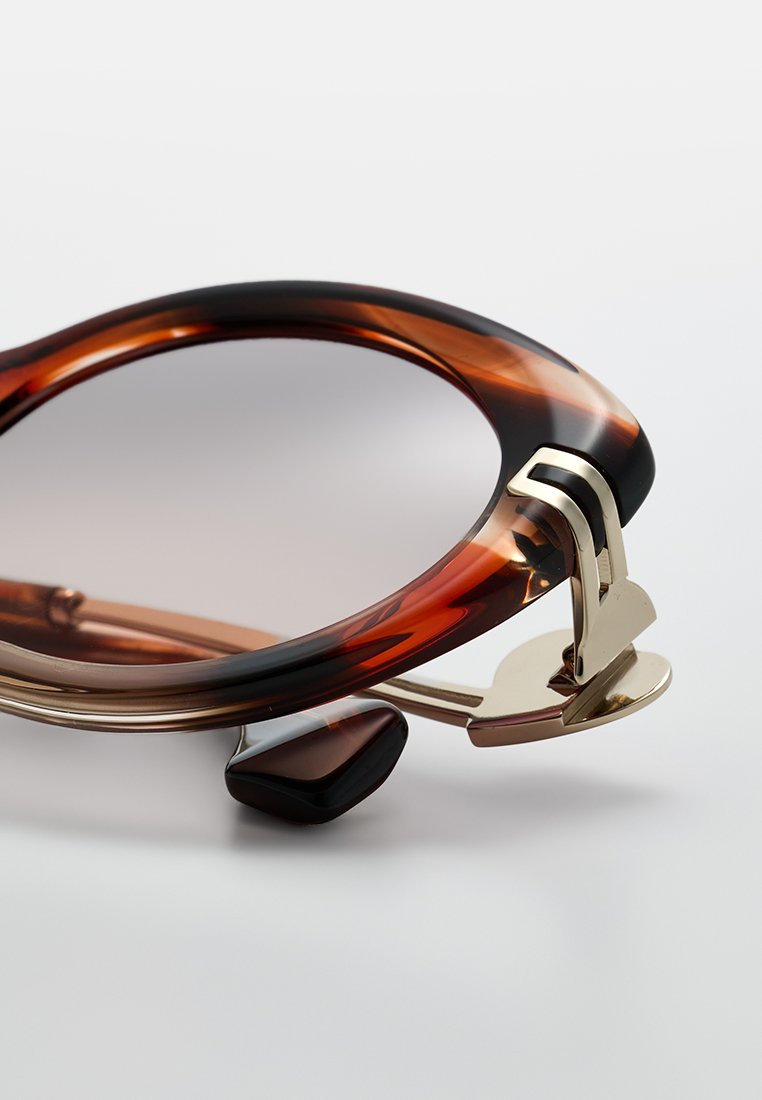 Schildpatt-Sonnenbrille mit einem goldenen Metallelement und einem schlanken, runden Rahmen. Die Gläser sind verlaufend, wobei sie von dunkleren zu helleren Tönen übergehen.