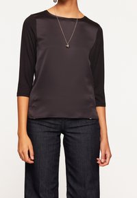 Černý dlouhý rukáv top s saténovým předním dílem a džersejovým zadním dílem. Výstřih je kulatý a jednoduchý náhrdelník doplňuje celkový vzhled. V kombinaci s tmavými džíny.