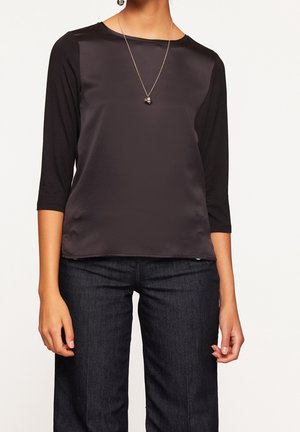 Top nero a maniche lunghe con parte anteriore in satin e retro in jersey. La scollatura è rotonda e una semplice collana completa il look. Abbinato a jeans scuri.