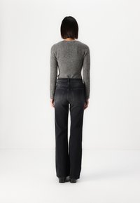 Grå strikkegenser med lange ermer, kombinert med høytlivs svarte jeans. Jeansene har baklommer og en rett, vid benklipp.