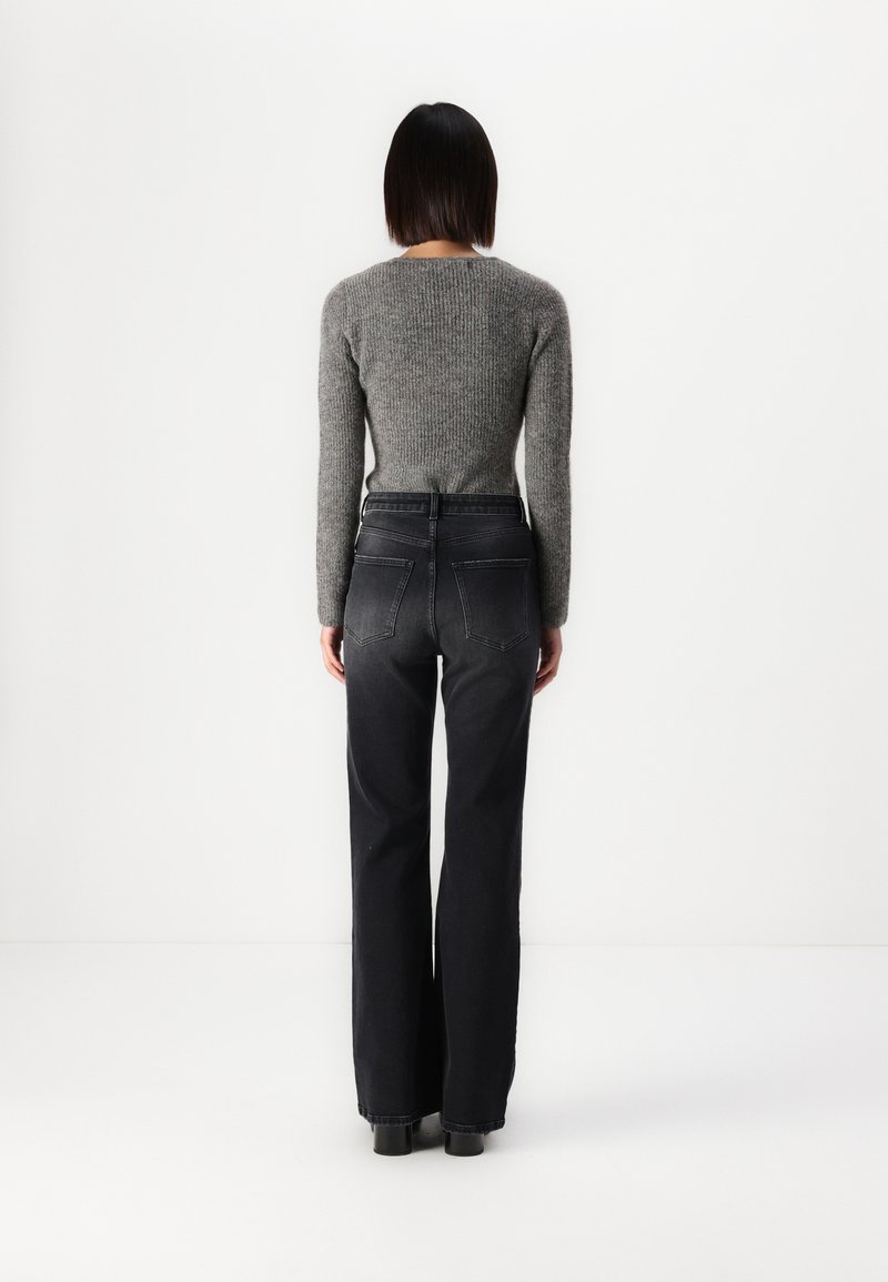 Maglione grigio a maglia con maniche lunghe abbinato a jeans neri a vita alta. I jeans hanno tasche posteriori e una vestibilità dritta e ampia.