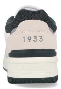 Tenisky Lacoste s vrchom z nubuku a sieťoviny, prevažne v béžovej farbe so sivými akcentmi, s číslom "1933" a čiernou gumovou podrážkou.