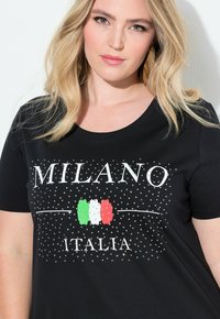 Černé tričko s textem "MILANO ITALIA", s tečkovaným vzorem a třpytivými akcenty. Italská vlajka je umístěna uprostřed.