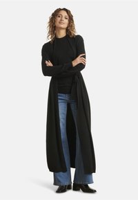 Black long cardigan with tie closure, worn over a black top and wide-leg denim jeans. Features soft fabric and open-front design.