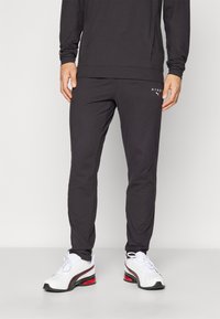 Svarta träningsbyxor med slim fit och mjuk textur, med en liten vit logotyp. Kombinerade med vita skor med röda detaljer.