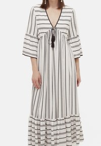 Dlouhé, volné šaty v bílých a černých pruhovaných barvách, s hlubokým výstřihem do V, nařaseným živůtkem, tkanicí s třásněmi a volánovým lemem.