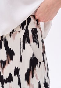 Pantalons légers présentant un motif abstrait noir et beige. Les poches latérales et une texture lisse complètent l'ensemble du design.