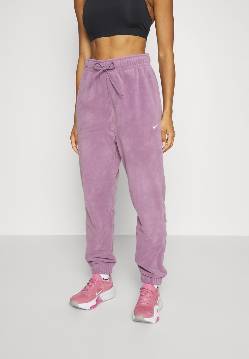 Lila Fleece-Jogginghose mit elastischen Bündchen und Kordelzug in der Taille. Kombiniert mit pinkfarbenen Sportschuhen mit weißem und pinkem Design.