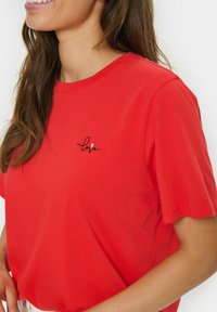 Red short-sleeve t-shirt made of cotton, featuring black embroidered text "love" with a small heart accent. Simple crew neck design.