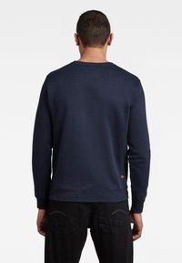 Marineblauer Pullover mit langen Ärmeln, Rundhalsausschnitt und weicher Textur. Verfügt über ein kleines Logoschild an der unteren Seite und gerippte Bündchen.