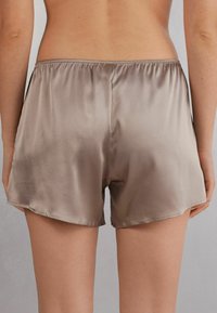 Shorts en satin dans une teinte beige atténuée, avec une coupe ample, une taille élastique et une texture lisse, avec un ourlet qui tombe juste au-dessus de la mi-cuisse.