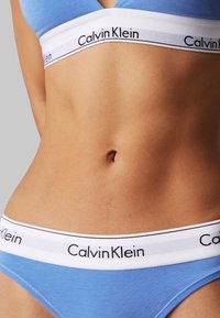 Calvin Klein blå bralette og briefsette med hvit elastisk midjebånd med svart logo, laget av myk, glatt stoff.