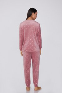 Měkký růžový sametový pyžamový komplet, který zahrnuje top s dlouhým rukávem a puntíky a odpovídající kalhoty, obojí s volným střihem a manžetami na lemech.