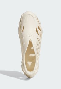 Cream-colored slip-on sneaker with a textured surface, cut-out patterns for ventilation, and an embossed logo on the insole.