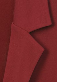 Gros plan sur des plis de tissu rouge montrant une texture de maille fine et des couches superposées de matière douce et lisse.