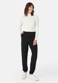 Sorte sweatpants med elastisk talje og sidelommer, parret med en tætsiddende hvid bluse med lange ærmer. Stoffet ser glat og blødt ud.
