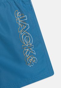 Blauwe zwembroek van lichtgewicht stof met een gedurfde "JACK&" grafiek in het wit en oranje. Voorzien van nette stiksels langs de randen.