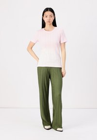 Světlá růžová ribovaná blůza s krátkým rukávem spárovaná se zelenými širokými kalhotami s sklady. Tento outfit má uvolněný střih a hladké textury.