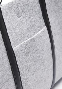 Grå tygväska med svarta läderdetaljer, med en framficka och rena linjer. Mjuk textur och strukturerad form.