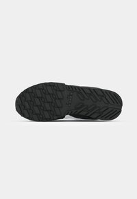 Black athletic shoe sole featuring a textured rubber surface with a zigzag pattern for grip, and a logo near the heel.