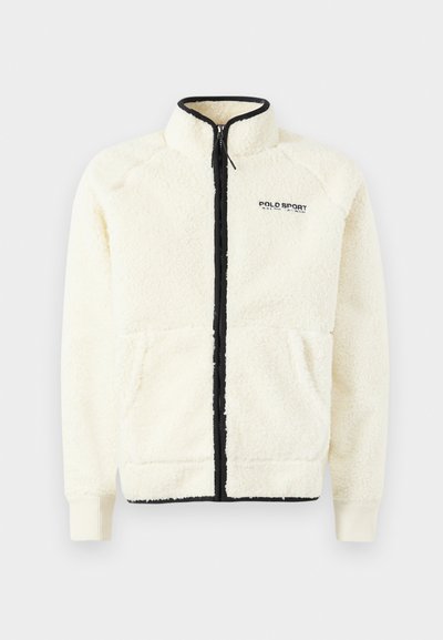 Krämfärgad fleecejacka med hög krage, svart dragkedja, två framfickor och detaljer med svart logga på vänster bröst.