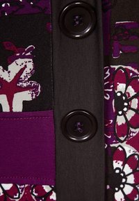 Gros plan sur des boutons brun foncé sur un tissu aux motifs floraux et abstraits en violet, blanc et noir.