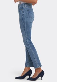 Ljusblå denimjeans med hög midja, smal passform, raka ben och subtila ränder, kombinerade med marinblå mockahöga klackar.