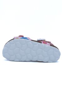 Sandales roses avec des accents floraux, semelle de pied texturée marron et semelle en caoutchouc blanche avec un design de grip à motifs.