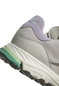 Ljusgrå mockaskor med lavendelaccent på hälen, grön mellansula, texturerad yta och svart gummisula.