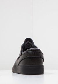 Svart lädersneaker med platt sula, rundad bakdel, minimal sömnad och subtil branding på insidan. Slät textur.