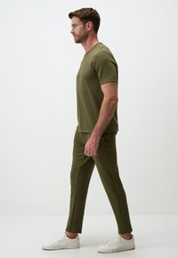 Olijfgroene t-shirt met korte mouwen gecombineerd met bijpassende getailleerde broeken, gemaakt van zachte stof. Gestyled met witte sneakers voor contrast.