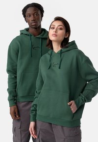 Sweatshirts verts avec cordons, poches avant et poignets côtelés. Dispose d'un logo noir brodé sur la poitrine. Coupe décontractée et matériau doux.