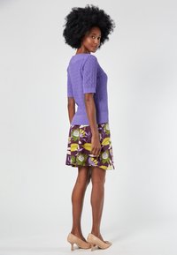 Purple knitted short-sleeve top paired with a floral-patterned skirt featuring purple, yellow, and green accents. Beige heels complete the look.