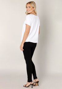 White short-sleeve top paired with black skinny jeans and black heeled sandals. Simple design, smooth fabric, and a relaxed fit.