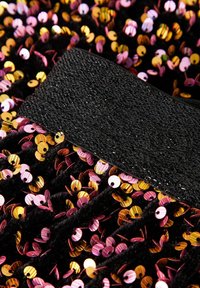 Tissu noir présentant une section texturée avec des sequins roses et dorés superposés, créant une apparence brillante et en couches.
