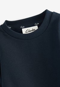 Sötétkék pamut póló bordás kerek nyakkal és "Clarks" felirattal ellátott címkével. Simább textúra, minimális dizájn.