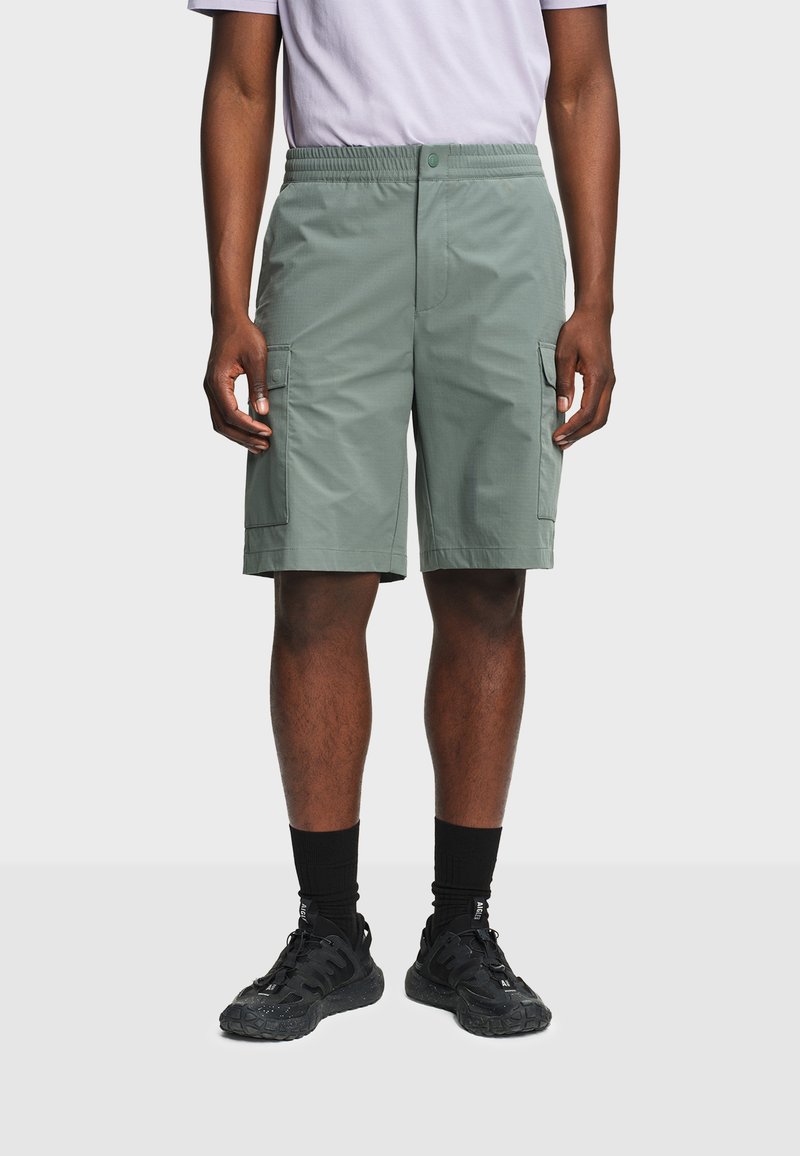 Homme portant un short cargo gris, des baskets noires et des chaussettes noires, debout les bras détendus le long du corps.