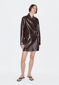 Bruine leren cropped jack met een kraag, vier knopsluitingen aan de voorkant en twee zijzakken; gecombineerd met een bijpassende bruine leren minirok.