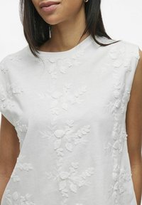 Top de algodón blanco con intrincados bordados florales blancos en la parte frontal, con mangas cortas y un escote redondeado.