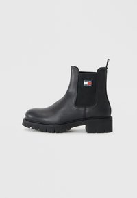 Bottine en cuir noir avec des panneaux latéraux élastiques, bout arrondi, tirant et semelle en caoutchouc épaisse, avec une étiquette logo sur le côté.