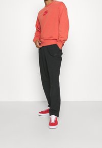 Červená mikina s logem Nike, spárovaná s černými kalhotami s kapsami a červenými teniskami s bílou podrážkou.