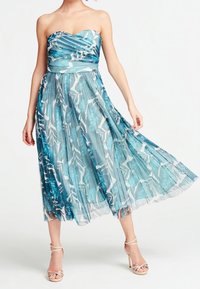 Robe midi sans bretelles, plissée, en tissu bleu transparent avec des motifs de feuilles blanches. Équipée d'un corsage ajusté et d'une jupe fluide, complétée par des talons nus à lanières.