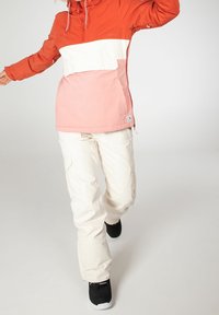 La chaqueta a bloques de color presenta paneles en naranja, blanco y rosa; combinada con pantalones cargo de color crema y calzado negro.