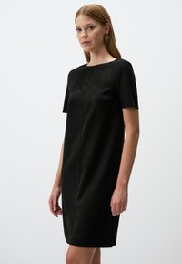 Zwart, kort mouwen jurk van zachte stof met een rechte snit. Heeft een ronde halslijn en minimalistische naaddetails.