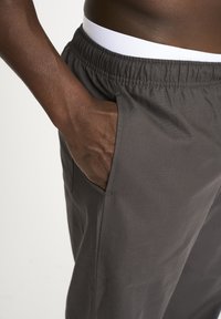 Gray athletic pants with an elastic waistband and a white inner band, featuring side pockets and a smooth, matte texture.