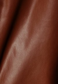 Bruin leer met een gestructureerd oppervlak, dat een lichte glans en subtiele patronen vertoont. Het materiaal is soepel en buigzaam, met natuurlijke kreuken.