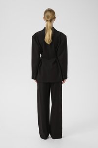Svart oversized blazers med strukturerte skuldre, parret med vide bukser. Glatt stoff med knappdetaljer på ermene.